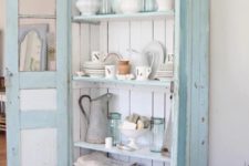 22 a pastel blue cupboard with white boards inside is used for storing dinnerware, pitchers and kitchen towels