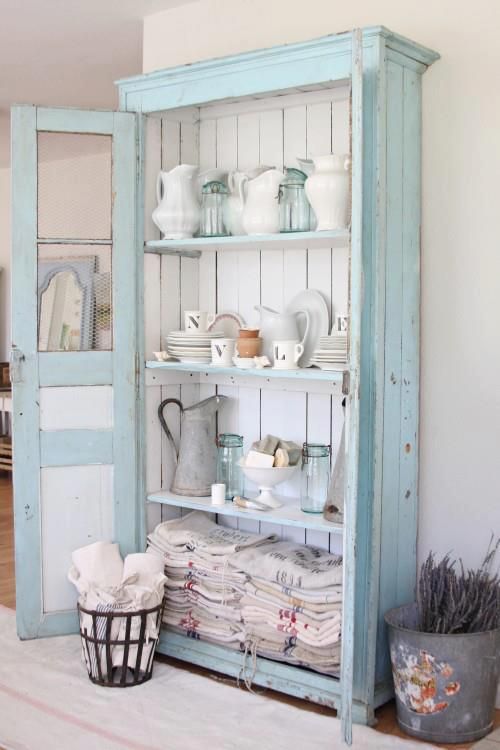 a pastel blue cupboard with white boards inside is used for storing dinnerware, pitchers and kitchen towels