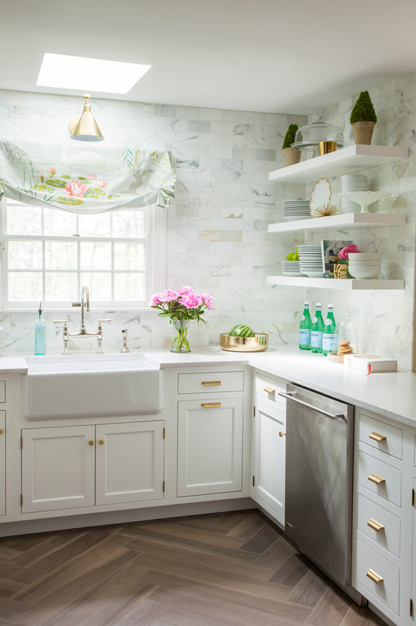 The walls are clad with marble subway tiles, there are white cabinets and floating shelves for comfortable and airy storage