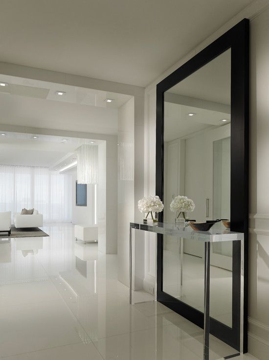 oversized wall mirror in a black frame defines the white entryway