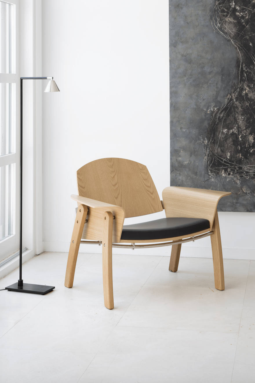 The Kimono chair is made of a leather cushion, light colored wood and a metal detail that holds the back