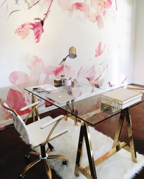 a glam trestle desk with brass legs and a glass tabletop and a matching brass and cream chair for a feminine space