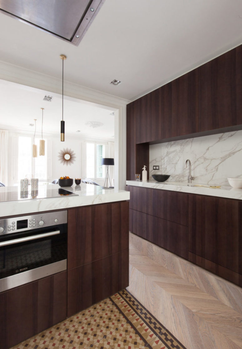 The kitchen features dark stained wooden cabinets and luxurious white marble countertops and a backsplash