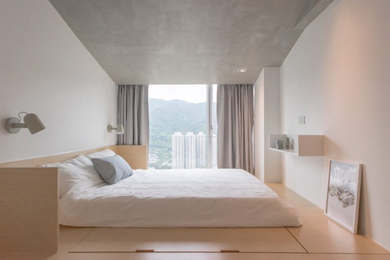 The master bedroom looks peaceful, with a concrete ceiling, adorable views and a bed on a platform