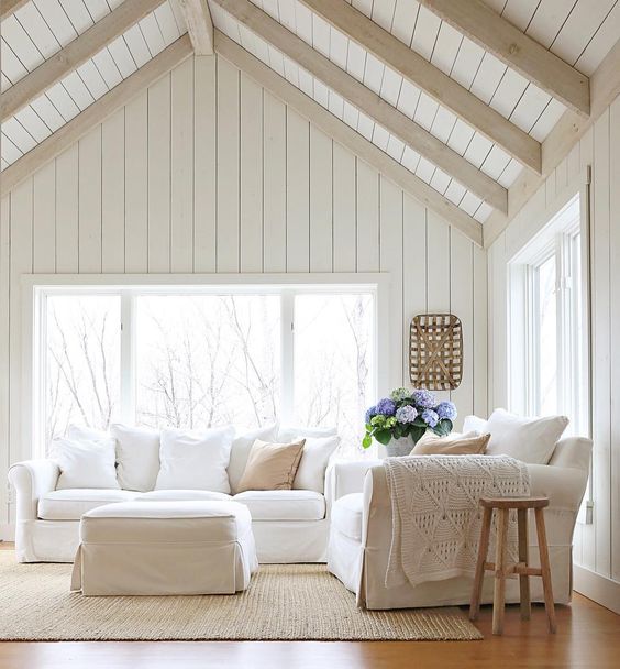a neutral living room is made cooler with whitewashed wooden planks that cover the ceiling and different textiles