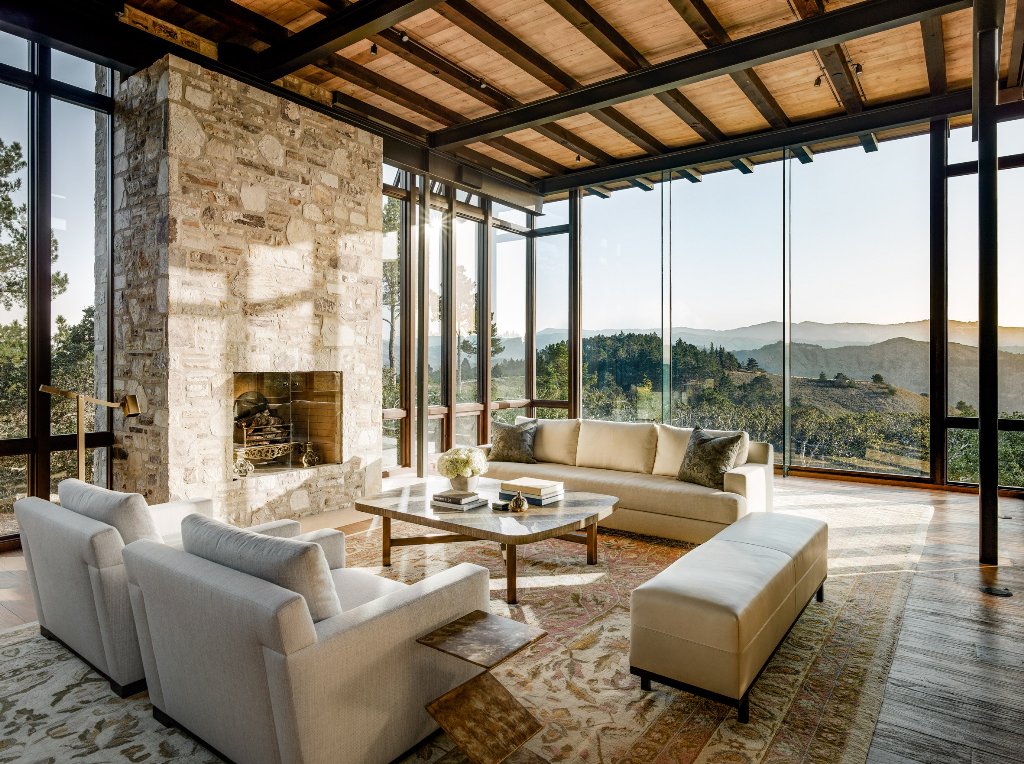 The living room is made with a stone fireplace and there's cozy cream upholstered furniture and glazings offer amazing views