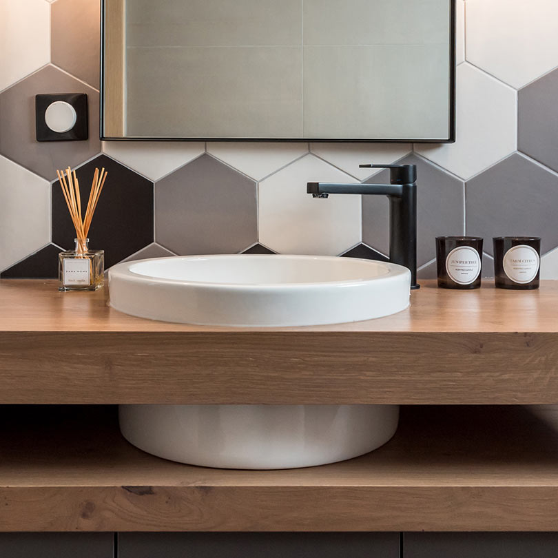 The powder room features a modern round sink in a double wooden vanity and hexagon tiles