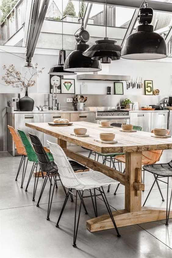 A modern industrial inspired space with colorful chairs is made warmer with a wooden table