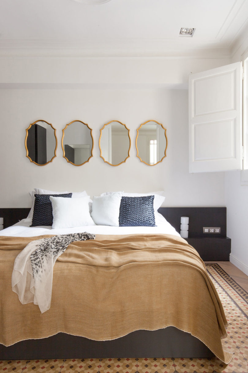 The master bedroom has vintage tile floors, a large upholstered bed and vintage framed mirrors instead of a usual headboard
