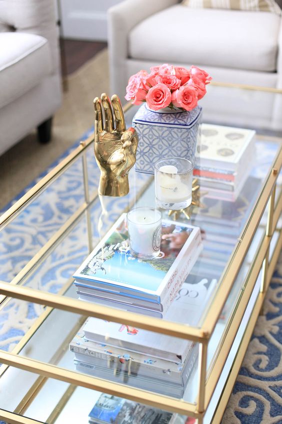 A glass three tiered coffee table with gilded framing offers storage and looks chic and glam