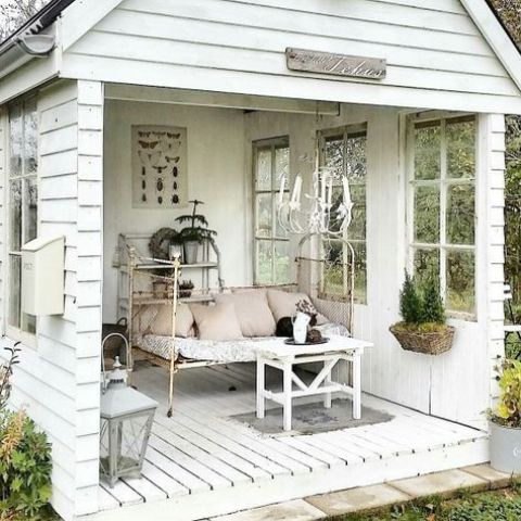 a shabby chic she shed in white, with a retro daybed, lanterns and some potted plants