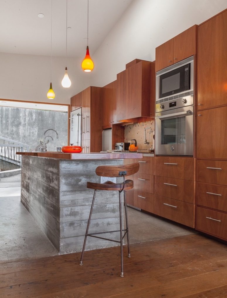 The kitchen is clad with warm-colored wood and there's a large kitchen island of concrete and wood
