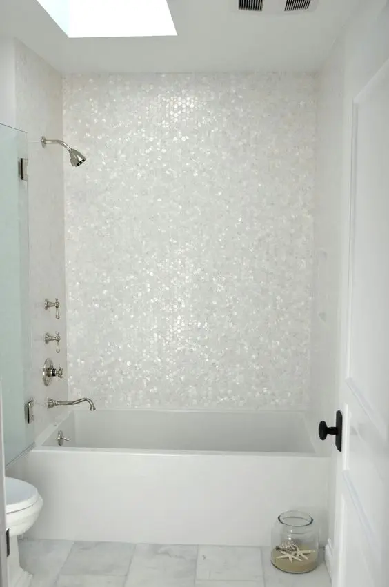 An all white bathroom is spruced up with hexagon mother of pearl tiles that make the bathtub zone stand out