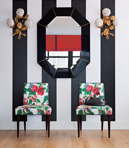 an art deco entryway in black and white is spruced up with bold green and red floral print chairs