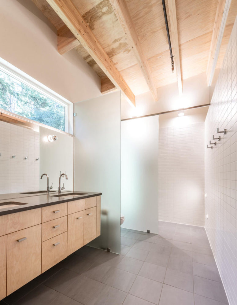 The bathroom is made cozier with light-colored wood furniture, and frosted glass dividers separate it into zones