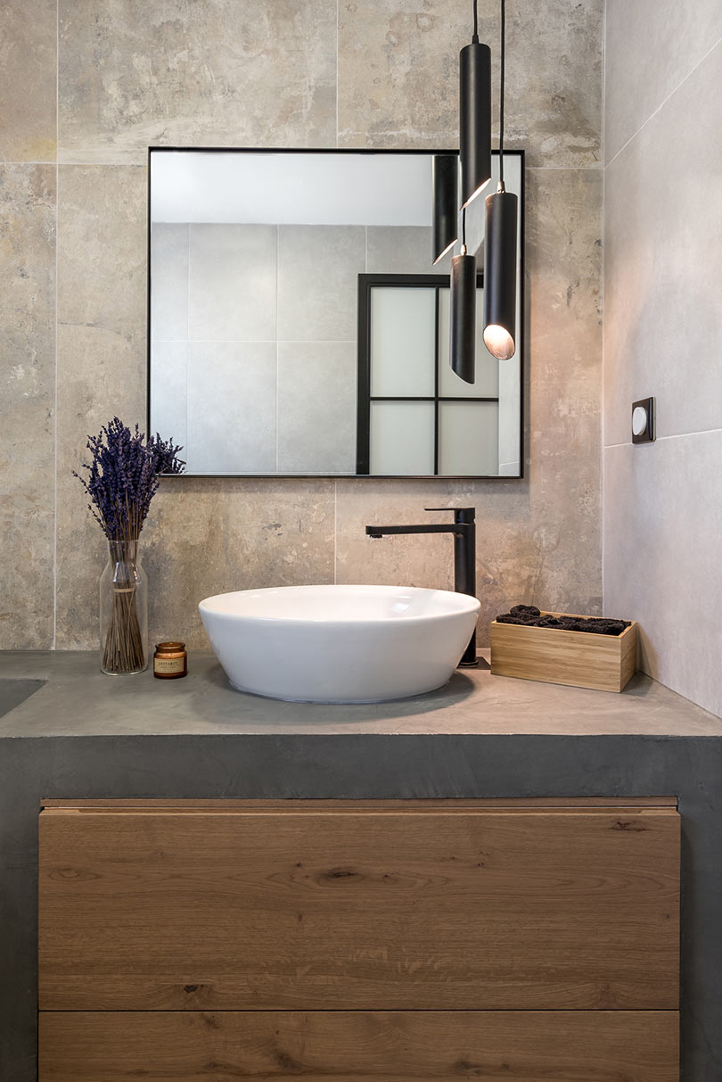 The master bathroom is clad with stone tiles, and the vanity is concrete, modern pendant lamps add a contemporary feel