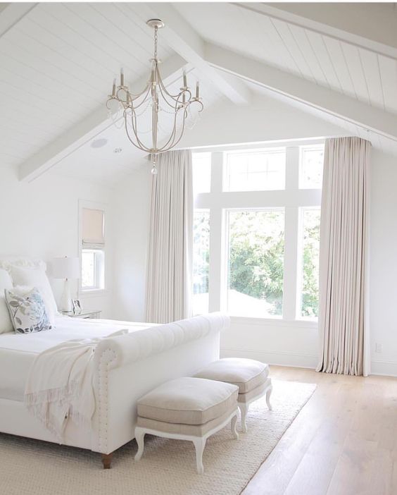 a white upholstered bed, curtains and a cozy rug add texture and comfiness to the bedroom