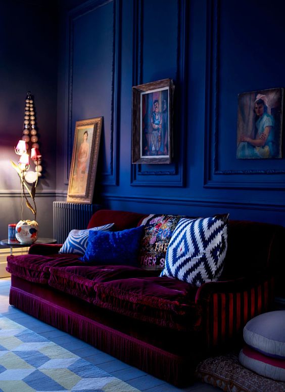 a moody cobalt blue space is made outstanding with a plum-colored velvet sofa