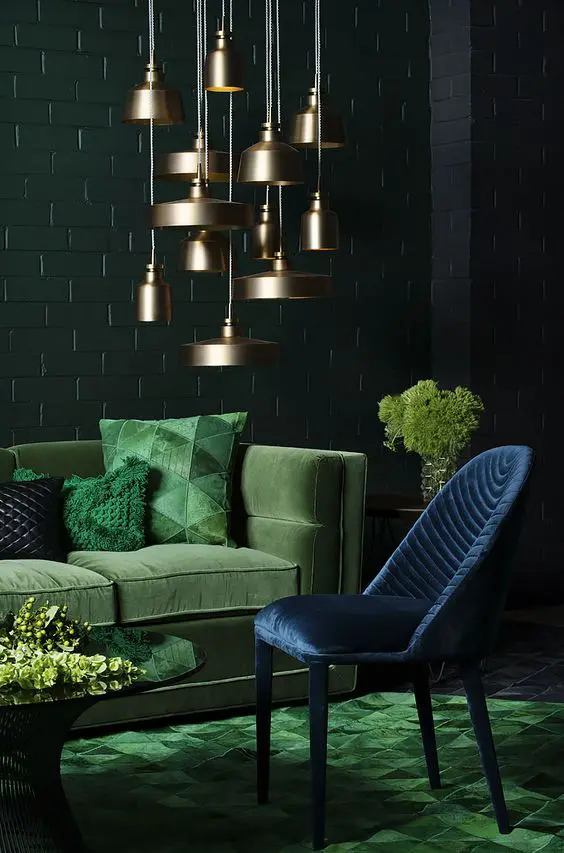 a moody space with a green velvet sofa and pillows and a navy velvet chair and brass lamps