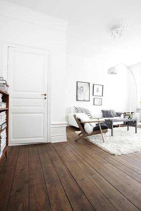 a white Scandinavian living room is made cool with dark stained wooden floors