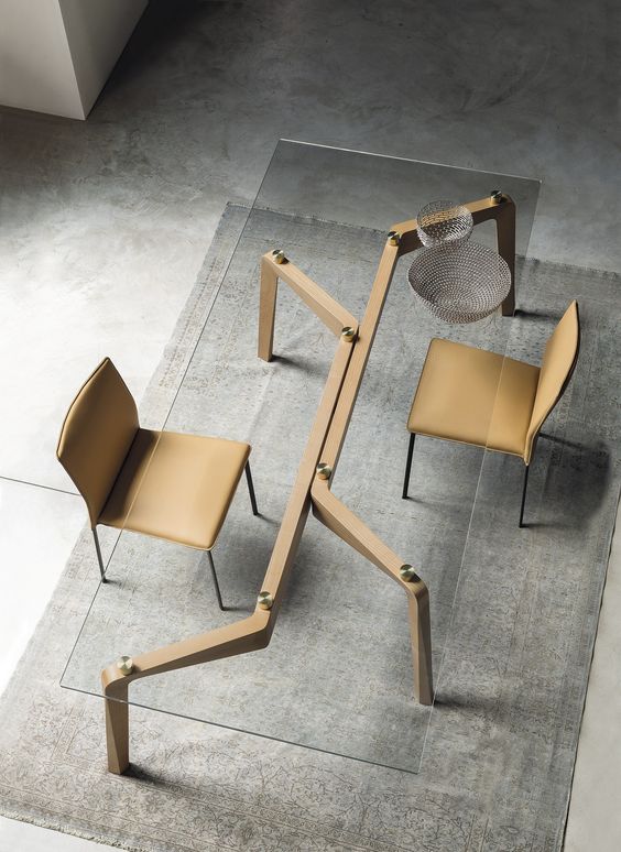a modern and industrial table on sculptural wooden legs, metallic touches and a glass tabletop, matching beige leather chairs