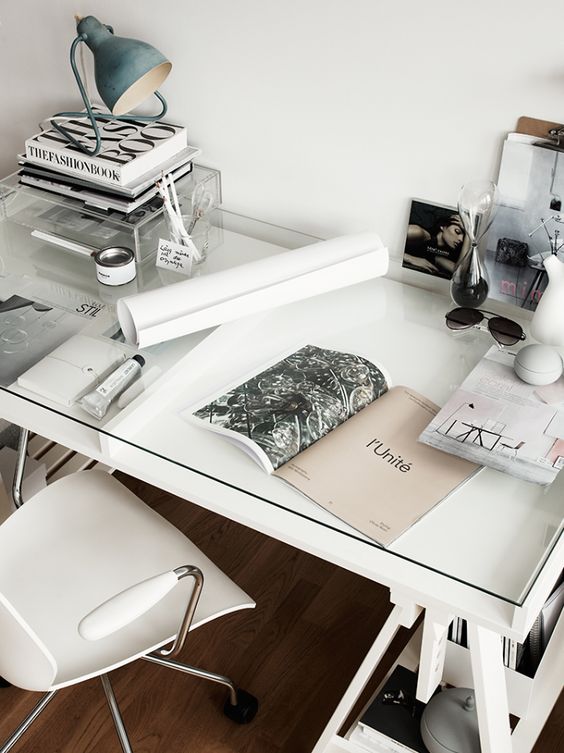 a Scandinavian home office with a white desk and a glass top over it to use the space inside for storage