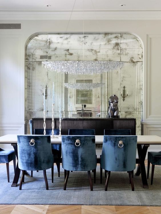 a modern dining room is made luxurious with a large crystal chandelier and an oversized faded mirror