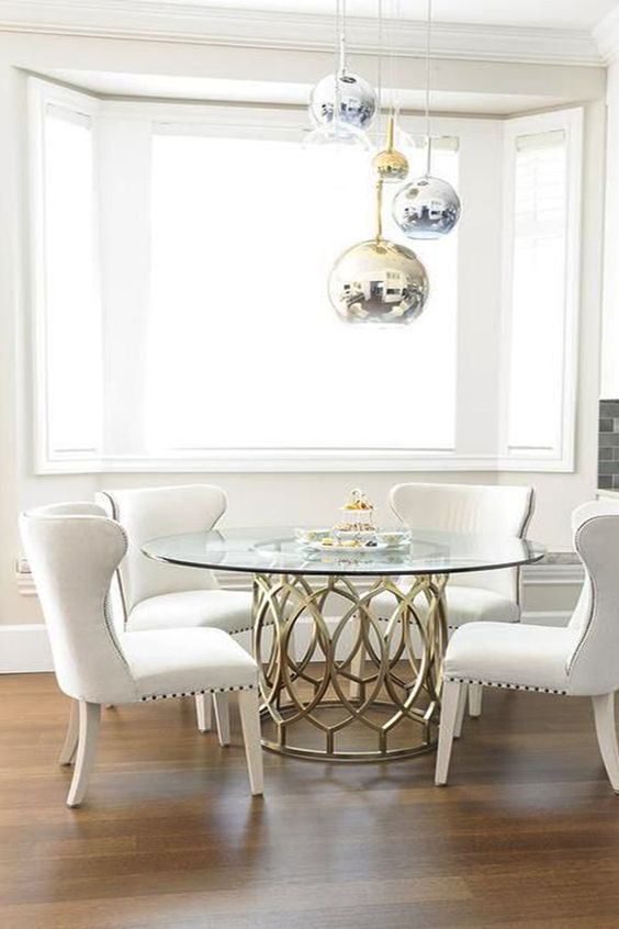 a glam dining space with metallic sphere pendant lamps, a brass table base and a round tabletop, comfy cream chairs