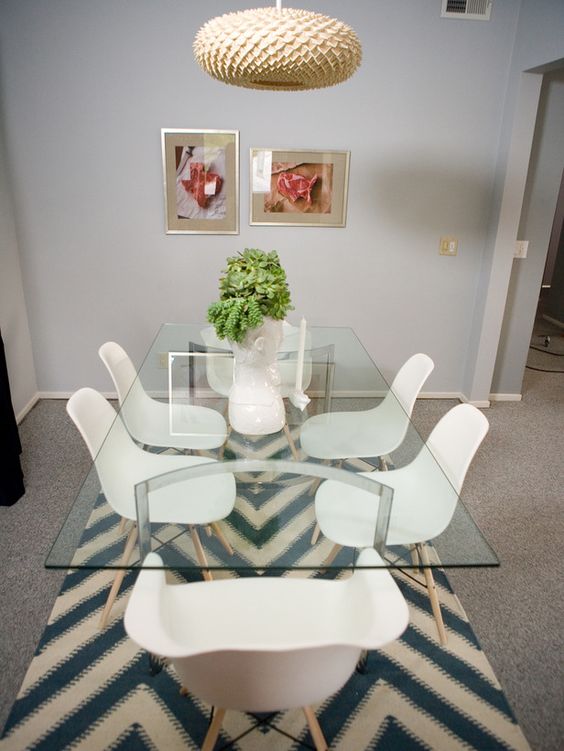 a glass top dining table with curved metal legs, modern white chairs and a creative pendant lamp