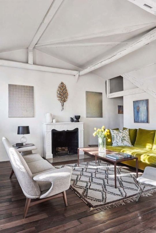 Most of the apartment is painted white, and there are wooden beams on the ceiling, the living room features an antique fireplace, comfy furniture and a statement - a mustard sofa