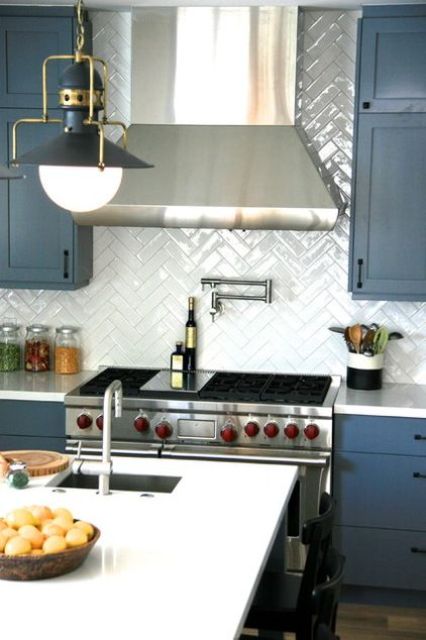 a glossy white tile herringbone backsplash makes the matte blue cabinets stand out