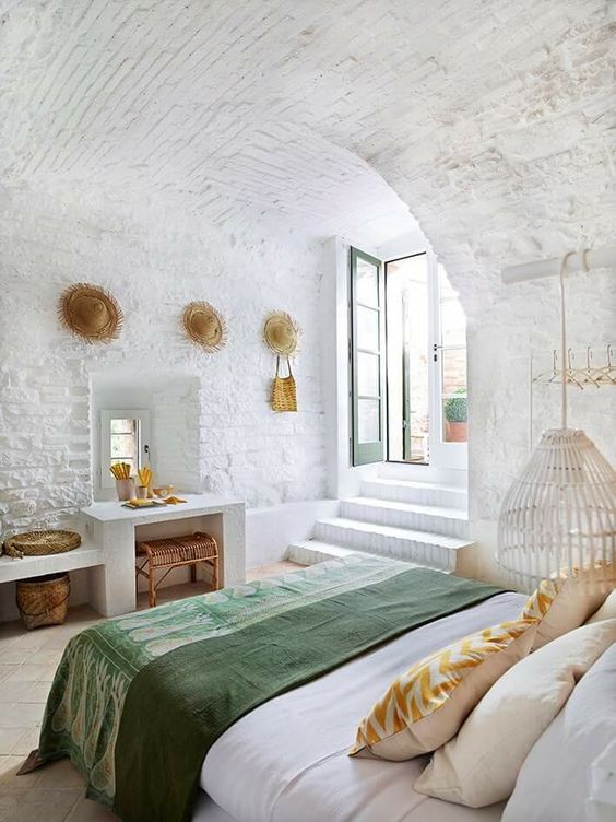 a mediterranean bedroom features whitewashed brick and tiles on the floor, everything is white except for bedding