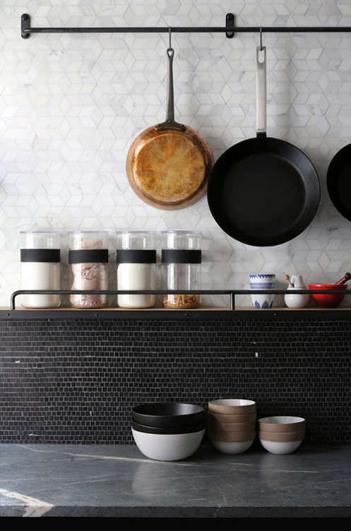 The kitchen backsplash is made with small black tiles, and the countertops are concrete