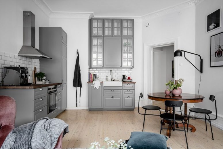 The kitchen is grey, with white subway tiles backsplashes and there's a small dining space with black chairs and a wooden table