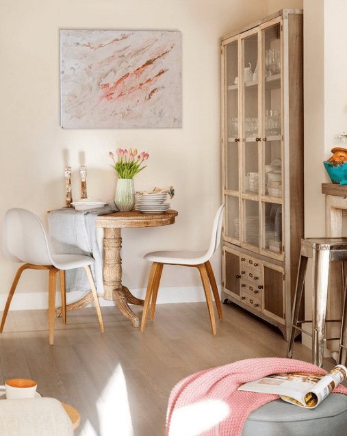 This is a tiny dining space with a round wooden table, modern chairs and a glass cupboard