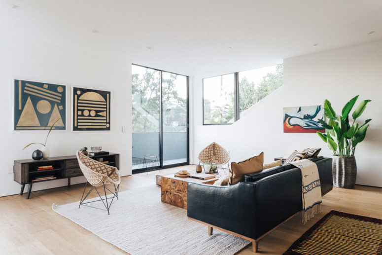 The living room is flooded with light from several windows, and makes a statement with a black leather sofa and more mid-century items