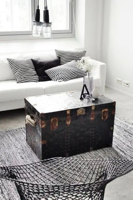 A Scandinavian room in black and white is ade more eye catchy with a black vintage trunk, which serves as a coffee table