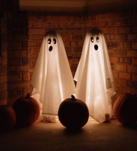 a couple of lit up ghosts with spooky faces and some pumpkins in the corner