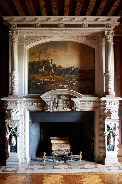 a gorgeous antique fireplace with pillars and a painting, with firewood that can be burnt or not