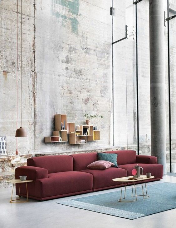 an industrial living room features a burgundy sofa and a muted blue rug for a contrast