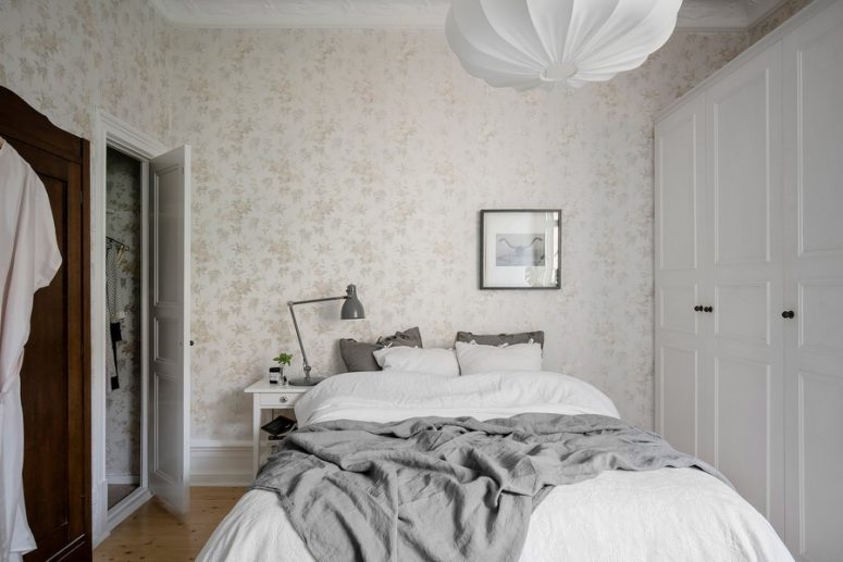 The master bedroom features neutral floral print wallpaper, a large comfy bed, wardrobes and wooden floors to create a cozy ambience