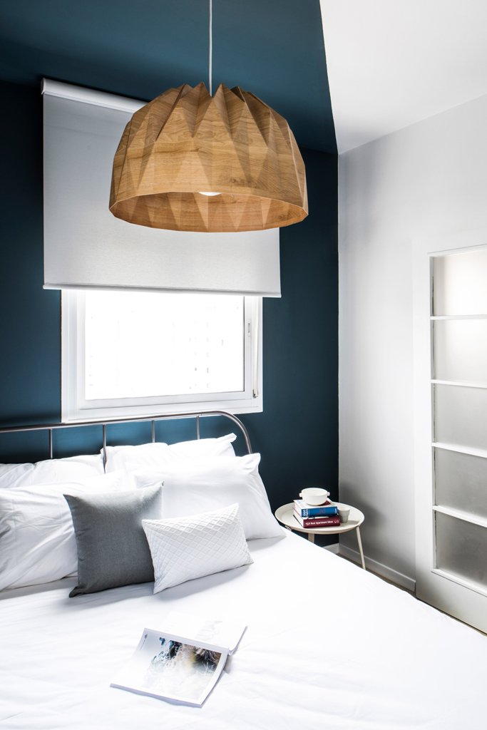 There's a large bed, a geo shaped wood lamp and a navy accent wall