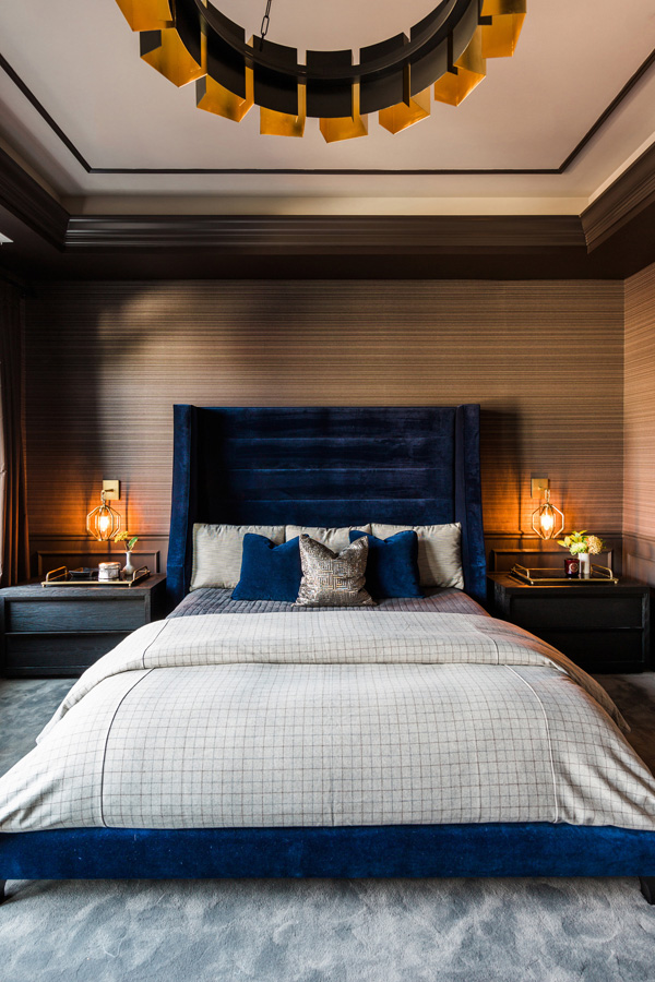 The master bedroom is moody and welcoming, with a blue velvet bed and art deco lamps