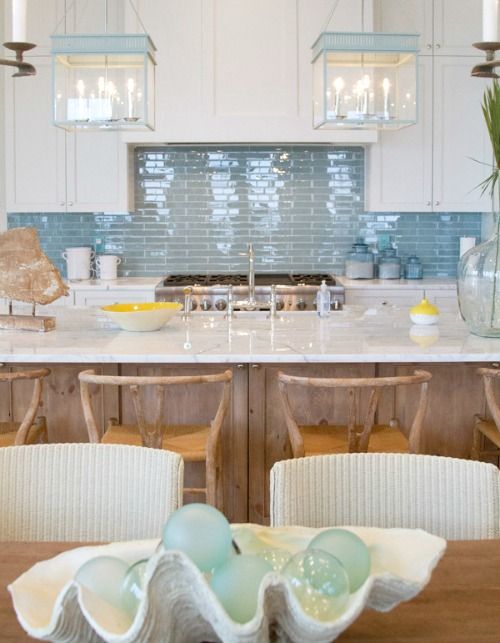 a seaside kitchen is made up using matte white cabinets and a glossy blue tile backsplash