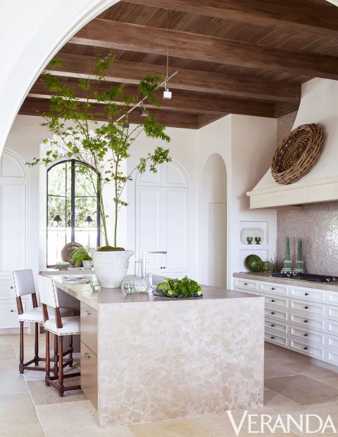 Spanish inspired ktichen in soft shades, with tiles and a rough wood ceiling with beams, a wicker basket on the hood