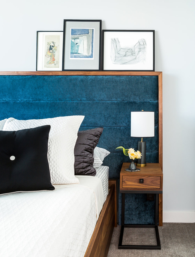 The bedroom has a large bed with an upholstered headboard and lots of artworks