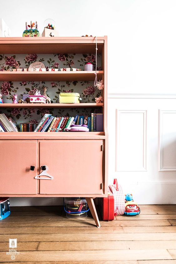 A coral colored sideboard with shelves and floral wallpaper inside for a kids' room