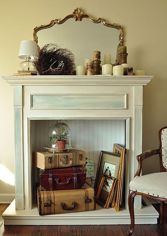 An antique fireplace is used for a vintage inspired display with suitcases, a cloche piece and paintings