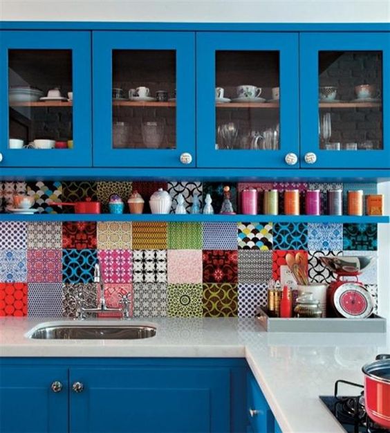 Bright colored blue kitchen with sleek white countertops and a bold assorted tile backsplash