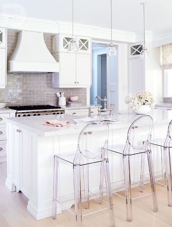 An all white kithen is spruced up with a glossy beige kitchen backsplash and acrylic chairs